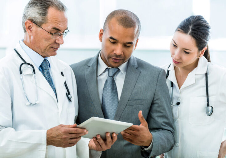 Two doctors and African American businessman using touchpad together.